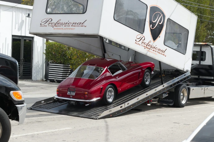 Red vintage car being loaded onto a car carrier.